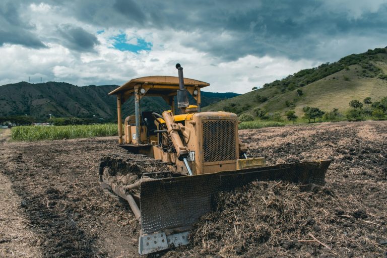 yellow and black heavy equipment on brown field under white clouds and blue sky during daytime